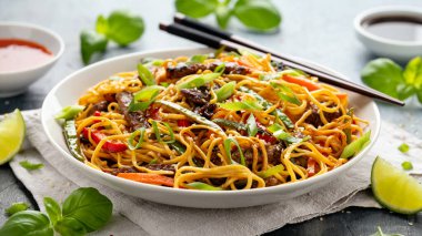 Kızarmış erişteyi sığır eti ve sebzeyle karıştırın. Asya usulü yemek.