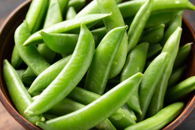 Çiğ organik yeşil şekerli bezelyeler ahşap kasede. Yemek için hazır.