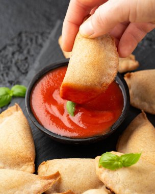 Margarita Margherita pizza paketleri domates, mozarella peyniri ve fesleğen ile dolu cepleri marinara sosu ve zeytin sosuyla birlikte siyah tahtada servis edilir. Parti yemeği.