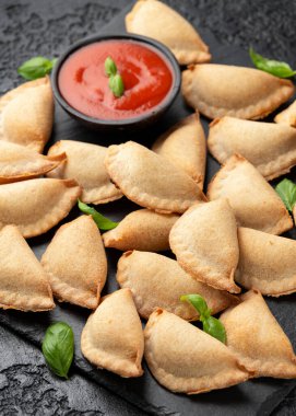 Margarita Margherita pizza paketleri domates, mozarella peyniri ve fesleğen ile dolu cepleri marinara sosu ve zeytin sosuyla birlikte siyah tahtada servis edilir. Parti yemeği.