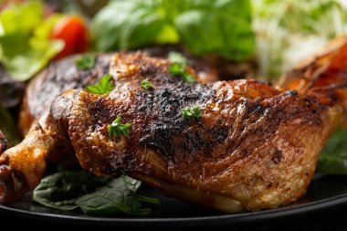 Yavaş pişmiş aromatik ördek bacağı, basmati pilavı ve siyah tabakta portakal dilimleri ile servis edilen salata.