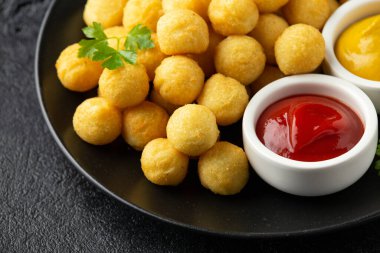 Ketçaplı çıtır patates topları ve siyah tabakta hardal.