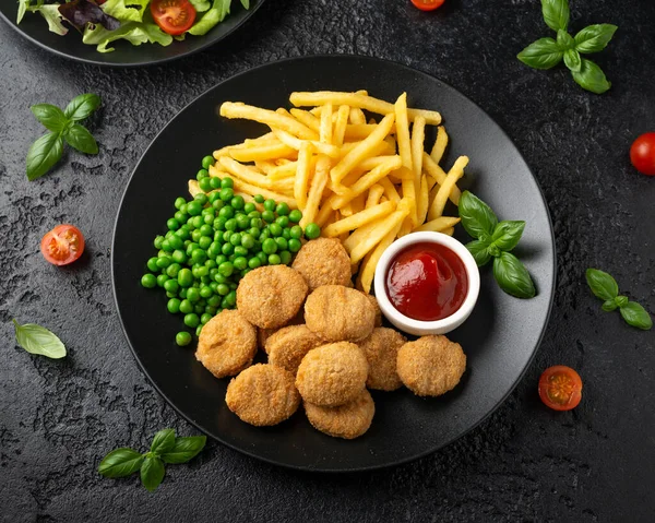 Nuggets de frango crocante frito com ketchup, batatas fritas e ervilhas verdes em prato preto — Fotografia de Stock