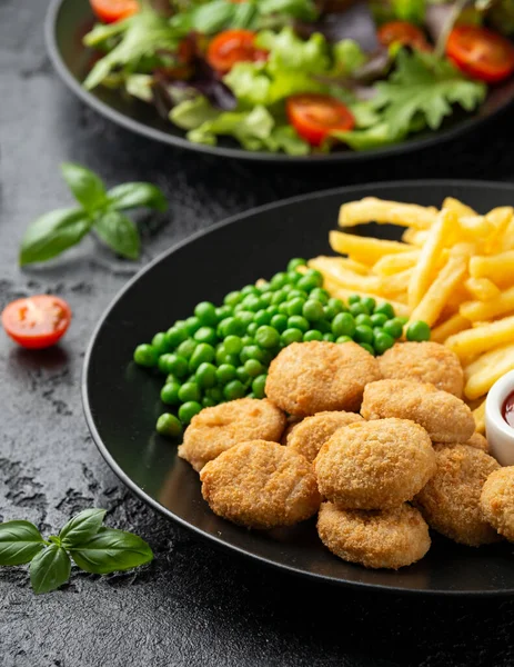 Stekt krispig kycklingnuggets med ketchup, pommes frites och gröna ärtor i svart tallrik — Stockfoto