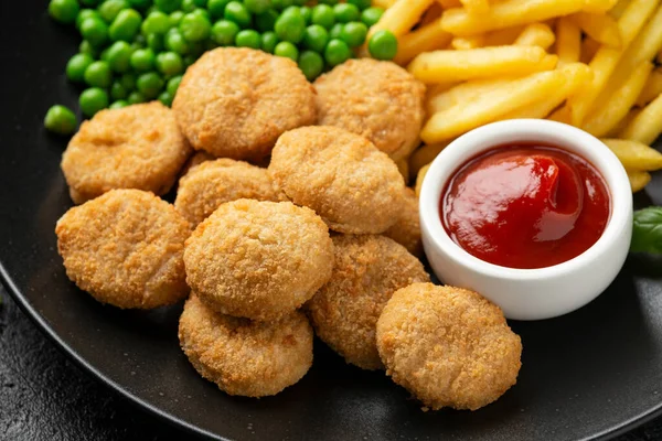 Fried crispy chicken nuggets with ketchup, french fries and green peas in black plate — Stock Photo, Image