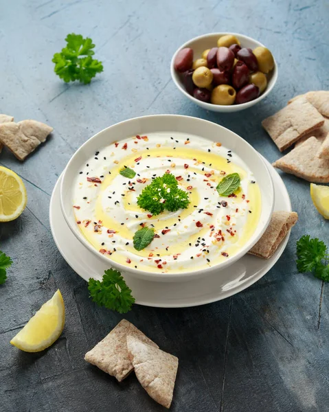 Labneh cremă brânză se înmoaie cu ulei de măsline, sare, ierburi servite cu măsline, pâine pita în castron alb — Fotografie, imagine de stoc
