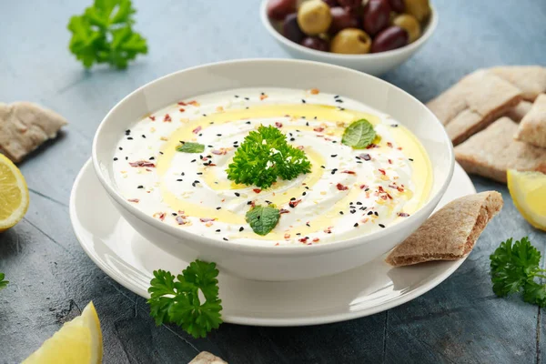 Labneh salsa de queso crema con aceite de oliva, sal, hierbas servidas con aceitunas, pan de pita en un tazón blanco —  Fotos de Stock