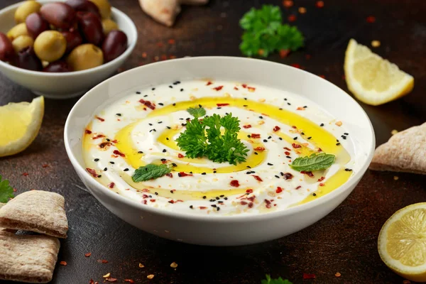 Labneh salsa de queso crema con aceite de oliva, sal, hierbas servidas con aceitunas, pan de pita en un tazón blanco —  Fotos de Stock