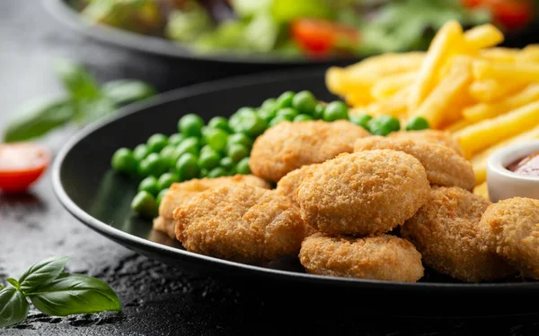 Gefrituurde knapperige kipnuggets met ketchup, frietjes en groene erwten in zwart bord — Stockfoto