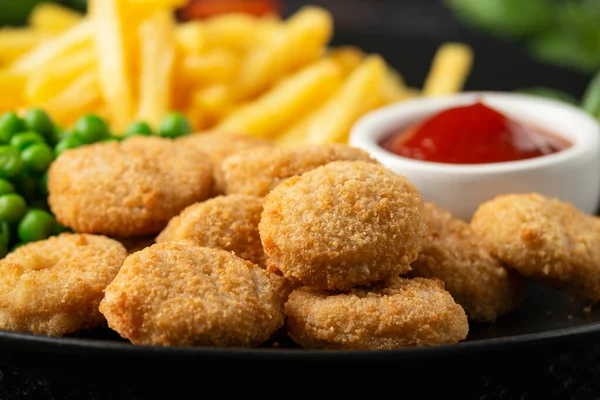 Gefrituurde knapperige kipnuggets met ketchup, frietjes en groene erwten in zwart bord — Stockfoto