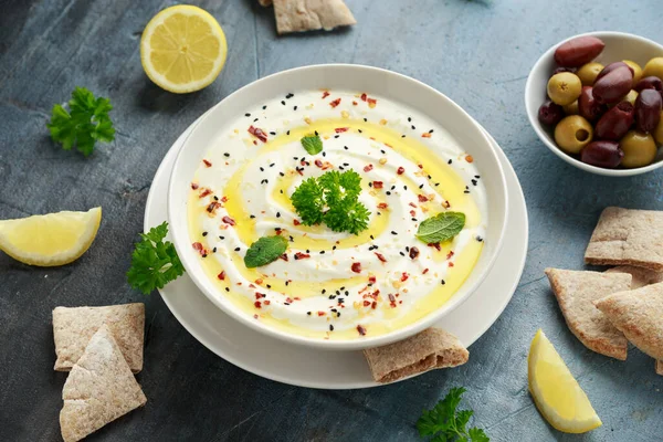 Labneh trempette au fromage à la crème avec de l'huile d'olive, sel, herbes servies avec des olives, pain pita dans un bol blanc — Photo