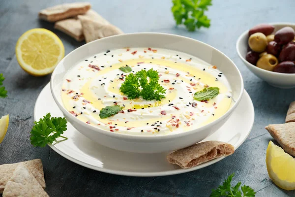 Labneh trempette au fromage à la crème avec de l'huile d'olive, sel, herbes servies avec des olives, pain pita dans un bol blanc — Photo