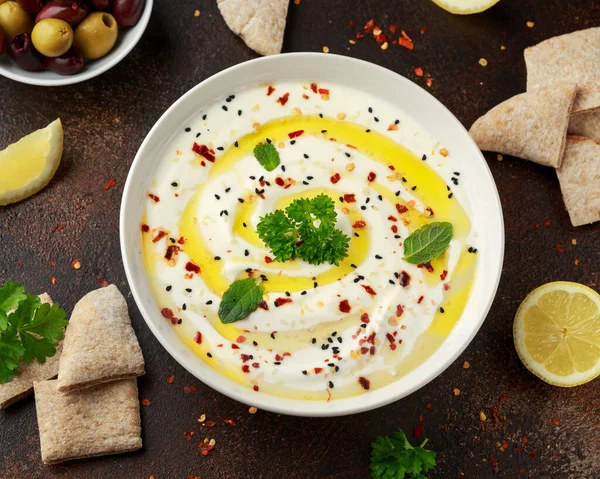 Labneh creme de queijo mergulho com azeite, sal, ervas servidas com azeitonas, pão pita em tigela branca — Fotografia de Stock