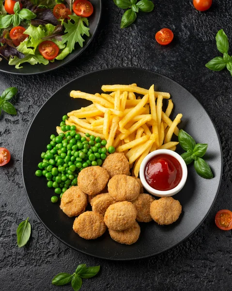 Stekt krispig kycklingnuggets med ketchup, pommes frites och gröna ärtor i svart tallrik — Stockfoto