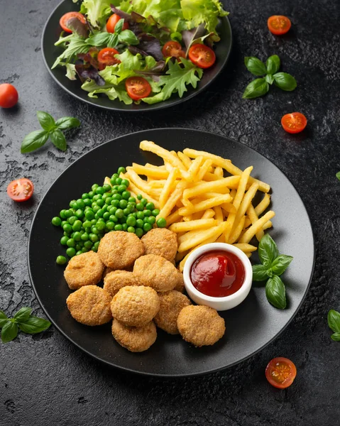 Gefrituurde knapperige kipnuggets met ketchup, frietjes en groene erwten in zwart bord — Stockfoto