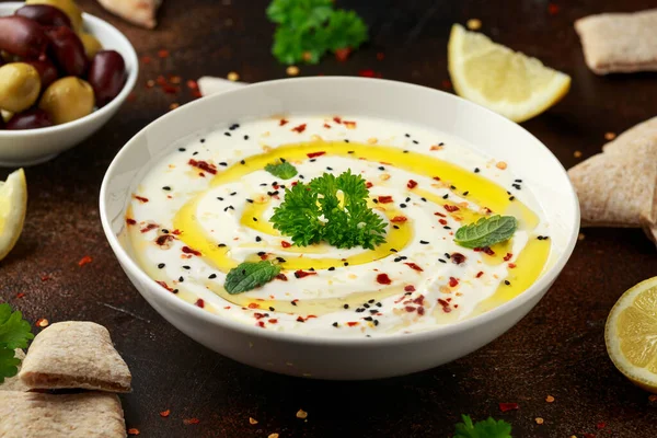 Labneh crema di formaggio tuffo con olio d'oliva, sale, erbe aromatiche servite con olive, pane pita in ciotola bianca — Foto Stock