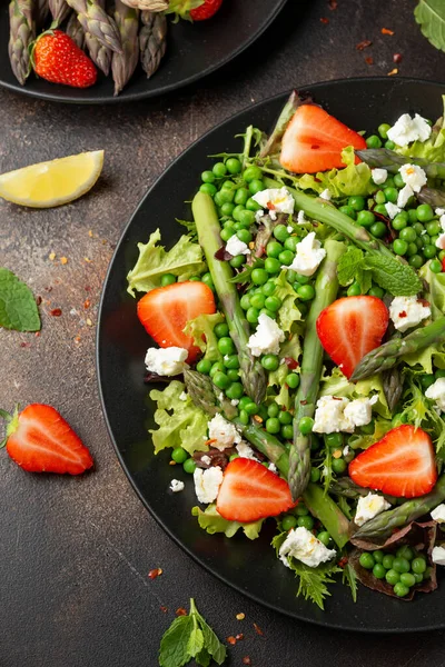 Салат зі спаржею та полуницею з овочами, зеленим горошком та сиром фета в чорній тарілці. здорова їжа . — стокове фото