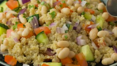 Kirazlı domates, salatalık, kırmızı soğan ve yemek kaşığı kullanarak tabaktan Quinoa beyaz fasulye salatası topluyorum. Sağlıklı vejetaryen yemeği. dönen video