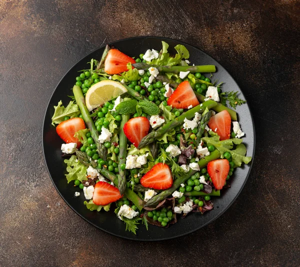 Салат зі спаржею та полуницею з овочами, зеленим горошком та сиром фета в чорній тарілці. здорова їжа . — стокове фото