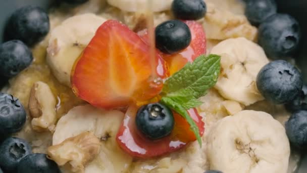 Micul dejun sănătos cu terci de ovăz cu căpșuni, afine, banane și miere. video rotativ — Videoclip de stoc