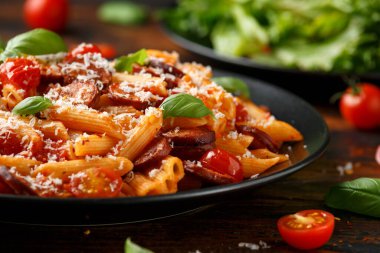 Domates soslu sosisli makarna, parmesan peyniri ve siyah tabakta fesleğen.