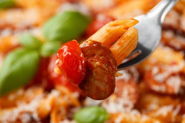 Domates soslu sosisli makarna, parmesan peyniri ve siyah tabakta fesleğen.