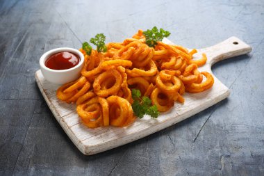Beyaz tahta üzerinde ketçaplı baharatlı kıvırcık patates kızartması.