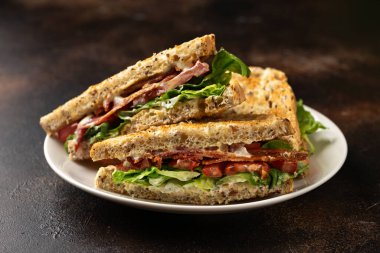 Beyaz tabakta salamlı ve domatesli taze BLT sandviçleri.