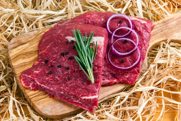 British Beef Flat Iron steak on cutting board and straw, rosemary and onion — Stock Photo, Image