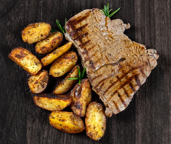 烤的牛肉牛排配烤烧烤村土豆、 旧木板迷迭香。背景纹理 — 图库照片