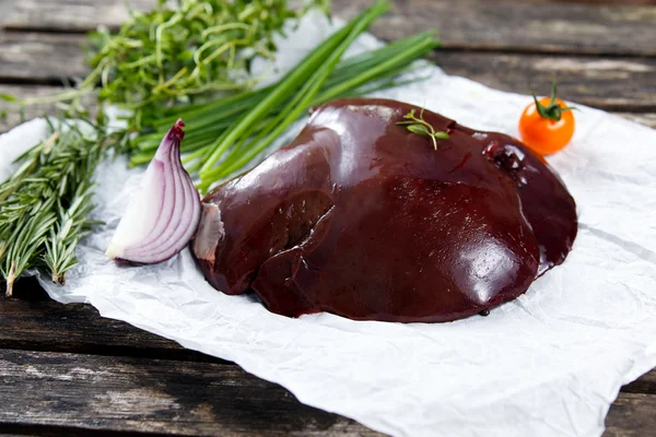 Fígado de cordeiro cru em papel amassado, decorado com verduras e legumes. na velha mesa de madeira — Fotografia de Stock