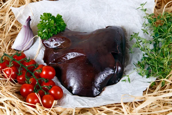 Raw Lamb liver on crumpled paper, decorated with greens and vegetables. — Stock Photo, Image