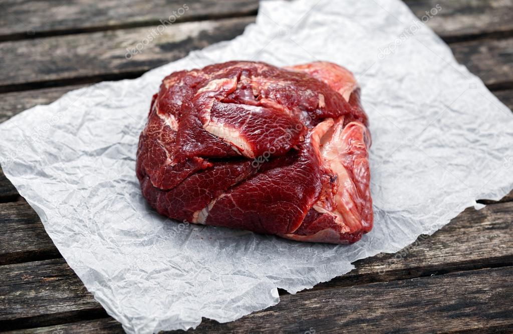 Raw Ox Cheek on crumpled paper,  on old  wooden table