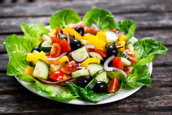 Ensalada de verduras frescas con, aceitunas negras, tomates cherry, pimiento amarillo, cebolla roja, pepino. Sobre mesa de madera —  Fotos de Stock