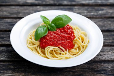 Spaghetti with marinara sauce and basil leaves on top, on wooden table.
