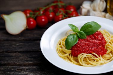 Spaghetti with marinara sauce and basil leaves on top, decorated with vegetables, olive oil. on wooden table.