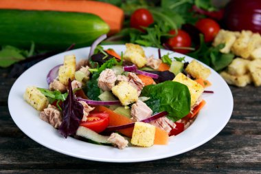Tuna salad with Spinach, rocket, red ruby chard, tomatoes, cucumbers, carrot, red onion, croutons on old wooden table.