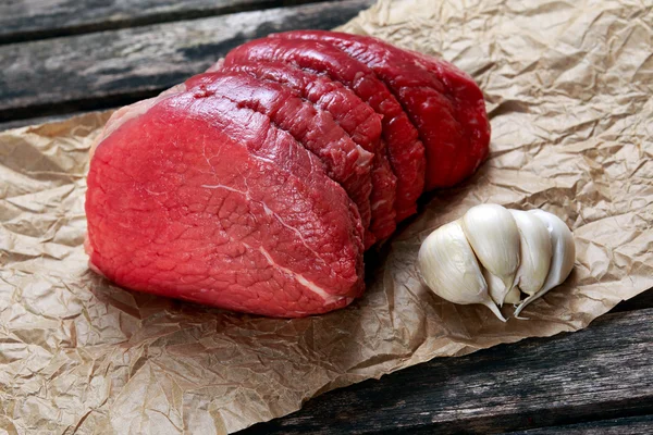 A pieces of fresh meat, beef slab on crumpled paper on old wooden table. ready to cook. — Stockfoto