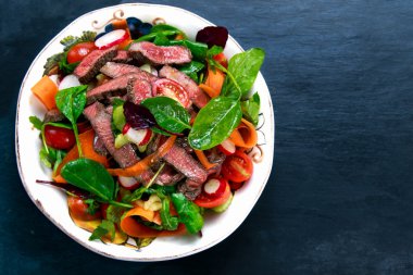 Spicy Beef Meat Salad with Carrots, Tomatoes, Cucumber, Parsley and Salad leaves Spinach, rocket, red ruby chard on old blue stone background.