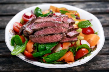 Spicy Beef Meat Salad with Carrots, Tomatoes, Cucumber, Parsley and Salad leaves Spinach, rocket, red ruby chard on old wooden table.
