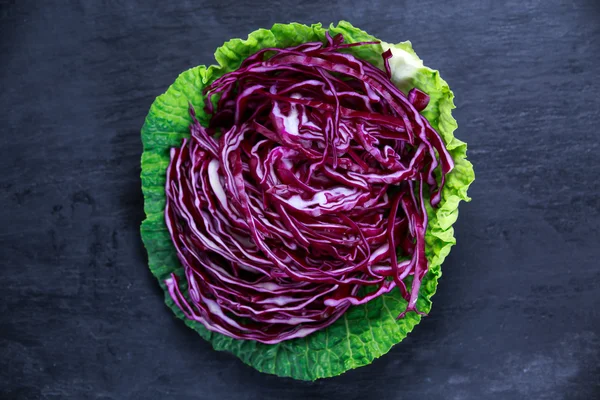 Fresh slices of red cabbage in green cabbage leaf on old blue stone background — Stock Fotó