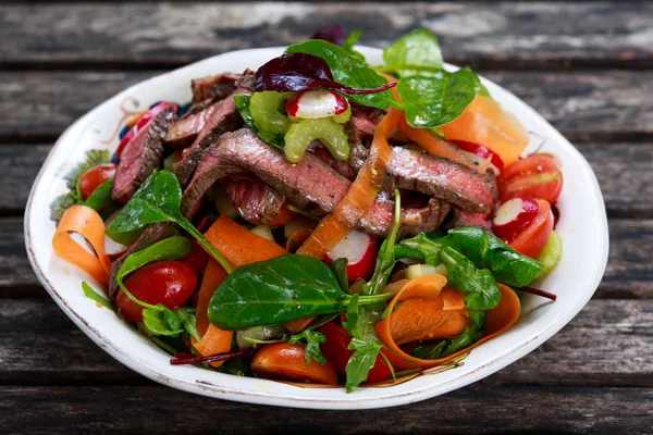 Spicy Beef Meat Salad with Carrots, Tomatoes, Cucumber, Parsley and Salad leaves Spinach, rocket, red ruby chard on old wooden table. — стокове фото