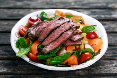 Baharatlı sığır eti dilim et salata havuç, domates, salatalık, maydanoz ve salata ile ıspanak, roket, kırmızı yakut pazı yaprakları eski ahşap tablo