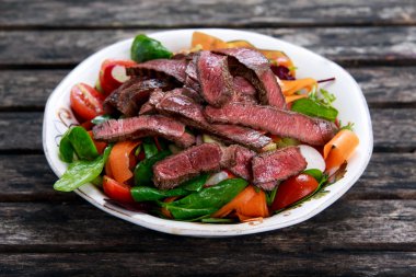 Baharatlı sığır eti dilim et salata havuç, domates, salatalık, maydanoz ve salata ile ıspanak, roket, kırmızı yakut pazı yaprakları eski ahşap tablo