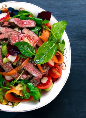 Baharatlı sığır eti dilim et salata havuç, domates, salatalık, maydanoz ve salata ile ıspanak, roket, kırmızı yakut pazı yaprakları eski mavi taş arka plan üzerinde