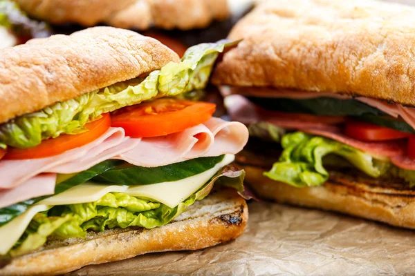 Sandwich a la parrilla con lechuga, rodajas de tomates frescos, pepino, cebolla roja, salami, jamón y queso . — Foto de Stock