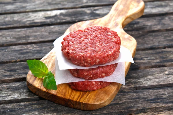 Hamburguesas de carne picada hechas a mano en la tabla de cortar. mesa de madera vieja . — Foto de Stock