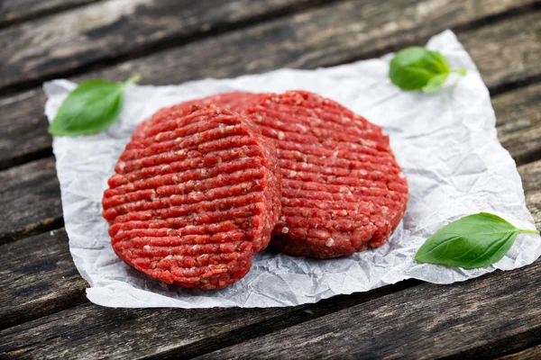 Hamburguesas de carne picada hechas a mano caseras decoradas con albahaca. sobre papel arrugado. mesa de madera — Foto de Stock