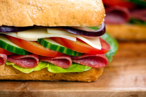 Sanduíche com alface, fatias de tomate fresco, pepino, cebola vermelha, salame e queijo — Fotografia de Stock