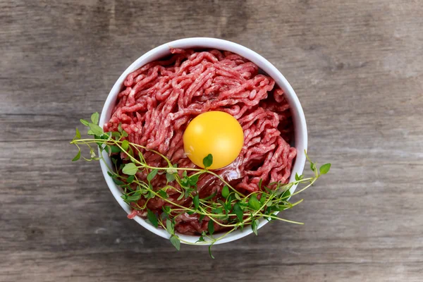 Carne fresca picada cruda con huevo sobre mesa de madera . — Foto de Stock